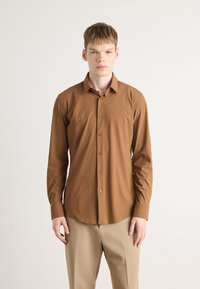 Camicia marrone a maniche lunghe in tessuto leggero con colletto a punta e patta frontale; presenta bottoni marroni e una vestibilità aderente.