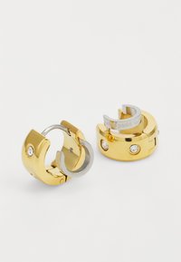 Orecchini in metallo dorato con un design chunky, caratterizzati da un accento argentato e dettagli in pietre gemme trasparenti. Chiusura a cerniera, forma circolare moderna.