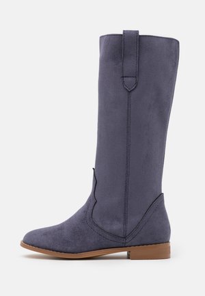 Botte en daim bleu marine haute avec un petit talon marron, bout arrondi et une languette en haut, sur fond blanc.