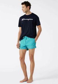 Ναυτικό μπλουζάκι με λογότυπο "Champion", σε συνδυασμό με τιρκουάζ βερμούδες κολύμβησης με ελαστική μέση και λογότυπο στο πλάι.