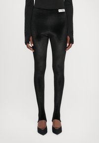 Black leggings made from a smooth, stretchy material, with a high waistband and a logo tag on the front. Subtle sheen texture.