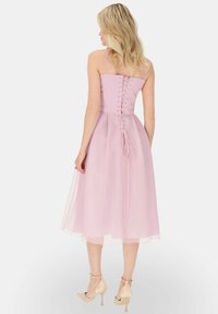 Różowa sukienka z szifonu z dopasowanym gorsetem, regulowanymi ramiączkami, szczegółami na plecach w formie sznurowania oraz zwiewną spódnicą kończącą się poniżej kolan. Neutralne szpilki.