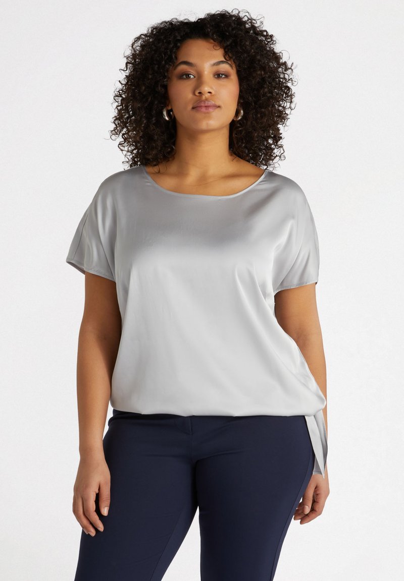 Blusa in satin grigia chiara con scollatura a girocollo, maniche corte e vestibilità morbida. Presenta un dettaglio di legatura laterale per un tocco di stile in più.