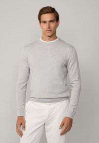Suéter de punto gris claro con mangas largas, escote redondo y puños y dobladillo acanalados. Combinado con pantalones blancos.