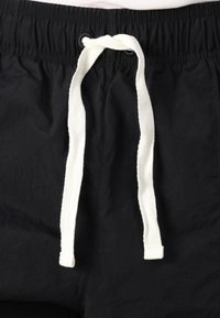 Black shorts made of lightweight fabric, featuring a white drawstring and elastic waistband. Smooth texture with no visible patterns.