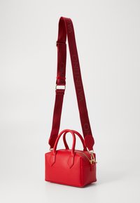 Punane tekstureeritud nahkrahakott, millel on tõmblukuga sulgemine, kaks käepidet ja reguleeritav rihm, millel on punase värviga trükitud "VALENTINO".