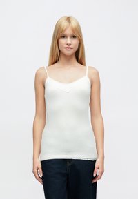 Hvit camisole-topp med tynne stropper, med blonderkant ved halsen og nederkanten, laget av et glatt, ribbet stoff.