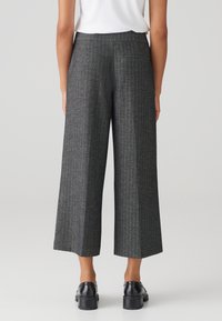 Grijze houndstooth wijde broek met een hoge taille, achterzakken en een gestructureerde stofafwerking. Gemaakt met zwarte schoenen.