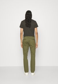 Chino verde oliva con gamba dritta e tasche posteriori, abbinati a una maglietta nera a maniche corte e sneakers bianche.