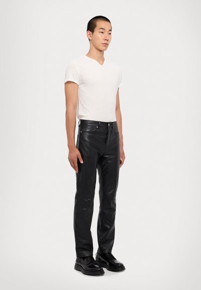 Pantalons en cuir noir à coupe slim, avec une fermeture éclair, des passants de ceinture et des détails de couture subtils, associés à une chemise V-neck blanche ajustée.