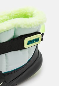 Nike boot featuring a soft neon green fleece lining, light blue nylon upper, black rubber sole, and a black strap with a green accent logo.