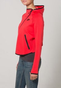 Red zip-up hoodie with black accents, slim fit, and high collar. Features a zippered pocket and thumbholes at sleeves. Made of soft material.
