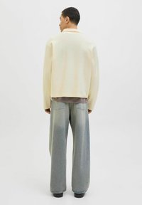 Une veste en tricot surdimensionnée de couleur jaune pâle avec un col, associée à un jean large bleu clair, vue de derrière.