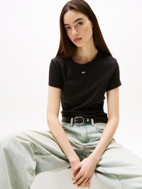 Svart fitted t-skjorte med korte ermer, kombinert med lyseblå, oversized denimjeans med belte med svart spenne og subtil merkevare.