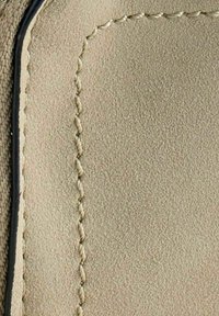 Nærbillede af beige læder med diagonal syning og sort kanttrim på en tekstureret overflade, der fremhæver materialets kvalitet og håndværk.