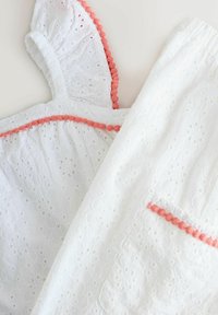 Hvid bomulds kjole med blomsterbroderi, der har flæser på ærmerne og koralfarvede pom-poms langs halsudskæringen og lommen.