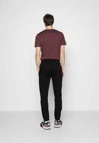 Maroon short-sleeve shirt, black tapered pants, and sneaker shoes. Smooth fabric, fitted design, and elastic waistband with a back pocket detail.