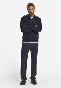 Marineblaues Strickpullover mit einem Reißverschlusskragen, gerippten Bündchen und Saum. Kombiniert mit dunklen, taillierten Hosen und schwarzen Slippern. Schlichtes und modernes Design.