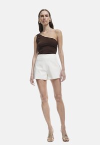 Top marrón de un hombro, pantalones cortos blancos con bordados florales y tacones dorados con tiras. Textura suave, diseño ajustado y corte entallado.