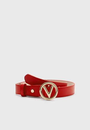 Ceinture en cuir rouge texturé avec une boucle ronde dorée présentant un « V » bien visible au centre, enroulée sur un fond clair uni.