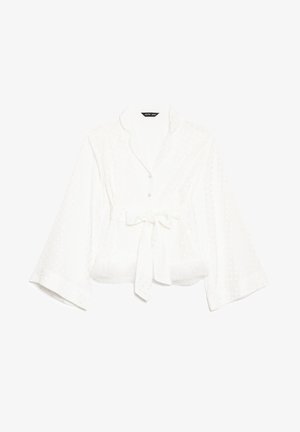 White long-sleeve blouse with subtle polka dot pattern, wrap style waist tie, and slight flare sleeves.