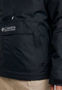Zwarte Columbia Sportswear jas met een gestructureerde stof, een voorzak met klep en een logodetail op de borst.