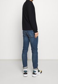 Svart långärmad tröja, blå slim-fit jeans och sneakers med vita, gröna, gula och svarta accenter; material av bomull och denim.