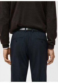 Ciemnobrązowy sweter na granatowych spodniach o gładkiej fakturze. Spodnie mają tylne kieszenie i czarny pasek, prezentując klasyczny design.