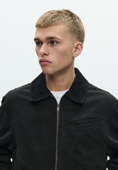 Μαύρο μπουφάν από τζιν με γιακά από κορντούρα, μπροστινό φερμουάρ και μικρή τσέπη στο στήθος. Λείο υλικό και casual εφαρμογή.