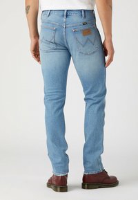 Jasnoniebieskie dżinsy o slim fit, z tylnymi kieszeniami z przyszytymi detalami oraz skórzaną metką przy pasku. Czerwone buty doskonale dopełniają całość.