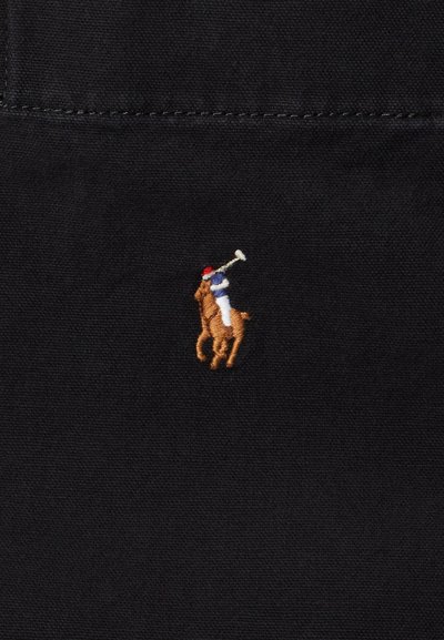 Tissu noir avec un petit joueur de polo brodé en marron et beige monté sur un cheval, tenant une mallette, souligné par un uniforme rouge et bleu.