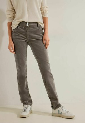 Personne portant un pantalon droit taupe avec fermeture à double bouton, un haut en maille gaufrée écru et des baskets blanches avec des accents bleu clair.
