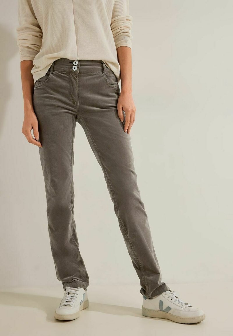 Personne portant un pantalon droit taupe avec fermeture à double bouton, un haut en maille gaufrée écru et des baskets blanches avec des accents bleu clair.