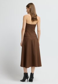 Hnědé bezramínkové šaty s upnutým korzetem a rozšířenou sukní, vyrobené z texturované látky. Kombinované s černými kotníkovými botami s zlatým akcentem.
