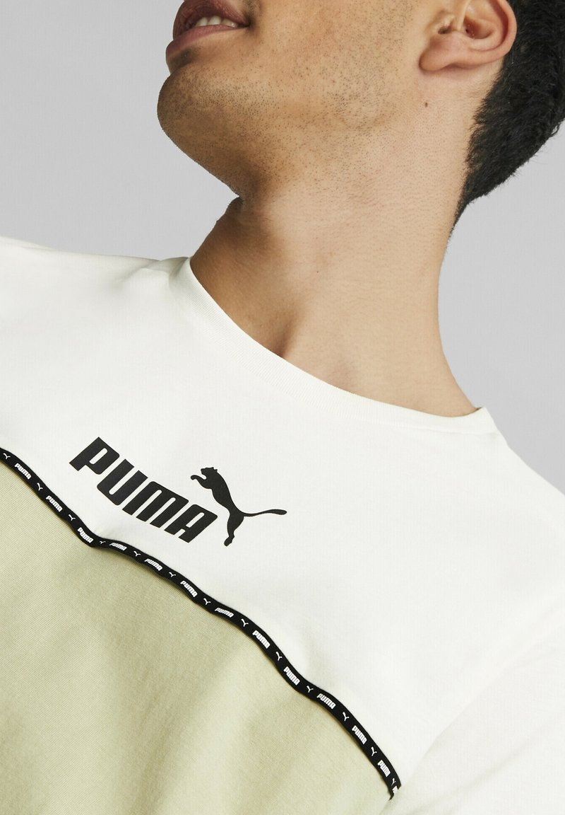 T-shirt bianco in cotone con un pannello inferiore verde. Presenta un logo PUMA nero e un bordo nero a motivo lungo la cucitura. Design con collo rotondo.