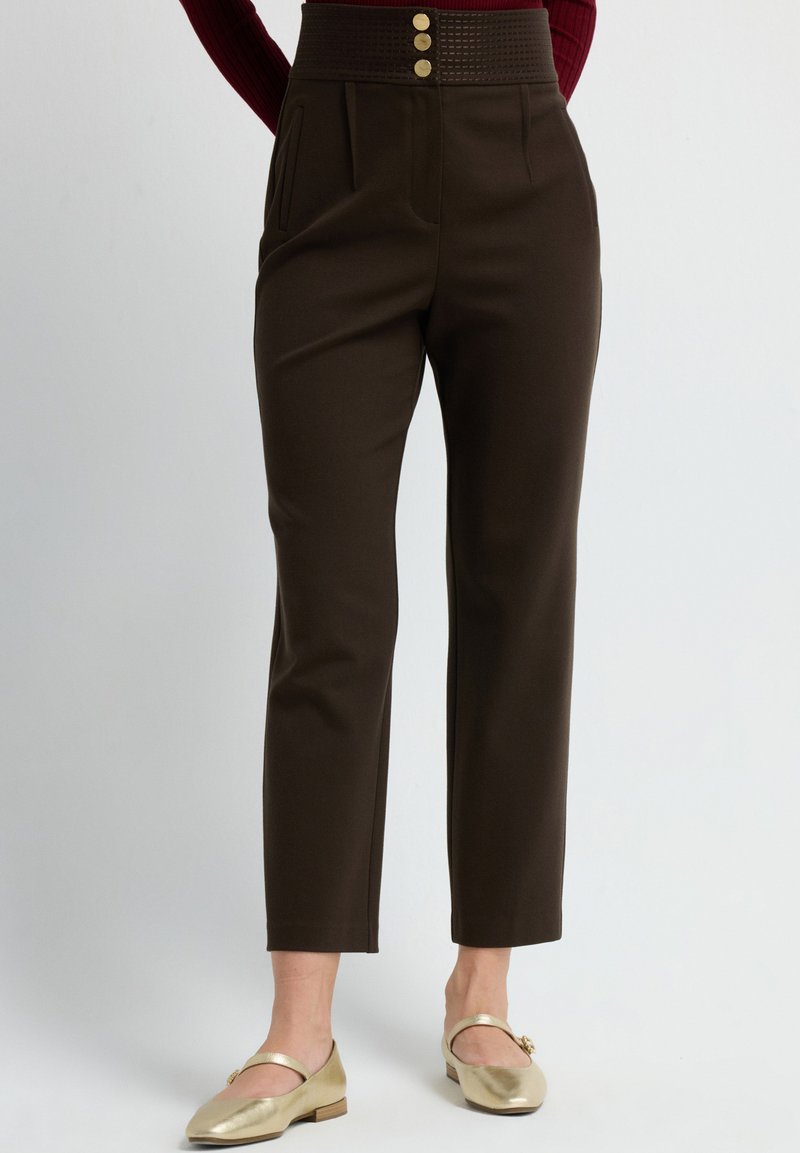 Pantalones marrones con una cinturilla alta que cuenta con tres botones dorados, pliegues y bolsillos laterales. La tela parece suave con un ajuste estructurado.