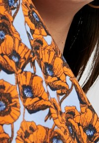 Motif floral orange sur un fond bleu, mettant en valeur de grands dessins de coquelicots avec des centres sombres. Le tissu semble léger avec une texture lisse.