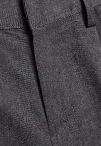 Gros plan sur un tissu gris, présentant une finition texturée avec un motif de tissage subtil et un pli au centre. Pas de quincaillerie ou d'accents visibles.