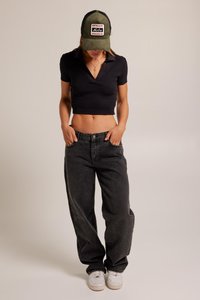 Black cropped polo shirt, oversized black jeans, and white sneakers. The cap is olive green with a front patch design. Minimalist style.