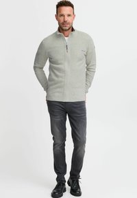 Vaaleanharmaa vetoketjullinen fleece-takki, jossa on teksturoitu pinta, yhdistettynä tummanharmaisiin farkkuihin ja mustiin nauhakengiin. Yksinkertainen muotoilu, käytännöllinen vaatetus.