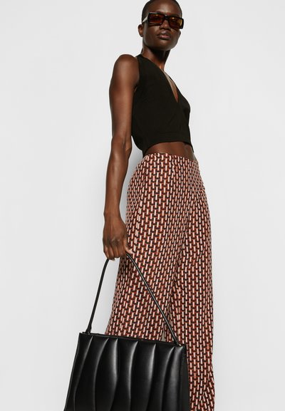 Top preto cropped, calças largas estampadas em tons de vermelho e castanho, e uma mala preta texturizada com um design simétrico.
