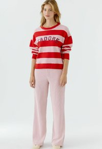 Pull rayé rouge et rose avec texte "JADORE" ; associé à un pantalon large à côtes rose clair. Tissu doux avec coupe décontractée.