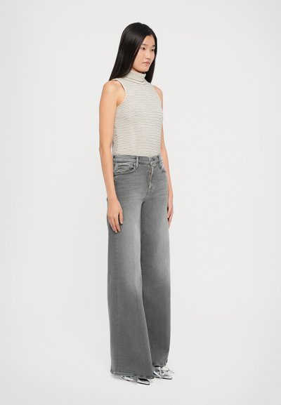 Striped, sleeveless turtleneck top paired with high-waisted, wide-leg gray jeans. Model wears metallic pointy-toed shoes.