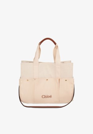 Sac fourre-tout en toile beige avec deux poignées supérieures et une bandoulière détachable, doté d'une poche avant et de quincaillerie dorée.