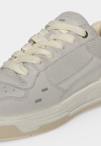 Baskets en daim gris clair avec lacets crème, panneaux latéraux perforés et semelle blanche avec bande de roulement beige.