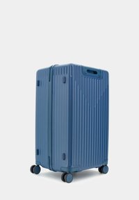 Valigia rigida blu con linee verticali in rilievo, maniglie integrate e quattro ruote nere per la mobilità. Materiale in plastica durevole.