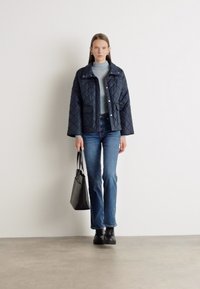 Καπιτονέ ναυτικό μπουφάν με κουμπώματα, δύο μπροστινές τσέπες, γκρι ζιβάγκο, μπλε τζιν, μαύρες ankle μπότες και γκρι τσάντα. Μινιμαλιστικός σχεδιασμός.