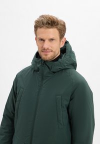 Dunkelgrüne, kapuzenjacke mit Reißverschluss. Verfügt über Seitentaschen und eine glatte, matte Textur. Einfaches Design und taillierte Passform.