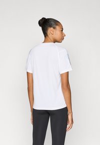 Fehér, rövid ujjú sportpóló bordázott mintával, kerek nyakkivágással és laza szabással, fekete, testhez simuló leggingsszel párosítva.