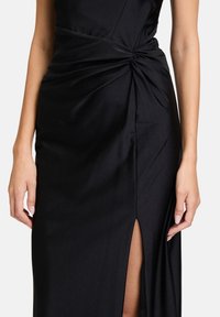 Schwarzes Kleid mit einem verdrehten Design an der Taille, versehen mit einem Oberschenkel-spalt und einer glatten Stofftextur, die elegante Linien betont.